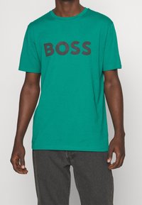 Grøn bomulds T-shirt med et stort sort "BOSS" logo på forsiden. Kortærmet og med rund hals. Enkel, afslappet stil.