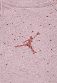 Lys rosa genser med en prikket tekstur. Har en rød Jumpman-logo brodert i midten. Mykt stoff, rund halslinning.
