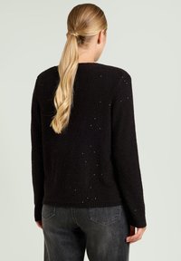 Maglione nero in maglia con finitura testurizzata, caratterizzato da piccole decorazioni. Ha maniche lunghe e scollo rotondo, con orlo a coste.