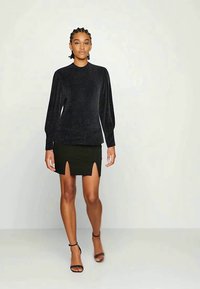 Top preto texturizado de manga longa combinado com uma saia mini preta justa com duas rachas frontais. Modelo usa saltos altos pretos com tiras.