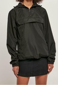 Svart lättviktspullov jacket med huva, halvdragkedja framtill, elastiska ärmslut och en framficka. Slät yta med avslappnad passform.