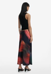 Black sleeveless top paired with a long, flowing skirt featuring a colorful abstract print in red, blue, and green hues. Flat black shoes.