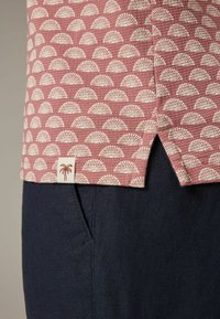 Chemise à manches courtes en tissu à motif de roses avec des formes éventail blanches, associée à un pantalon bleu marine, mettant en valeur les matériaux texturés et les détails.