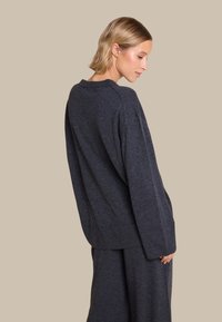 Mørk grå strikkegenser med lange ermer og avslappet passform, med rund halsringning og subtil ribbestruktur. Kombinert med matchende bukser.