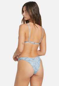 Modrý bikinový set so vzorom, ktorý obsahuje tenké ramienka, trojuholníkový vrch a spodný diel s minimálnym pokrytím, vyrobený z hladkej, elastickej tkaniny.