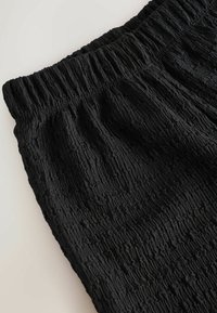 Primo piano di tessuto nero arricciato con una fascia elastica, che mostra un motivo testurizzato e materiale raggrinzito.