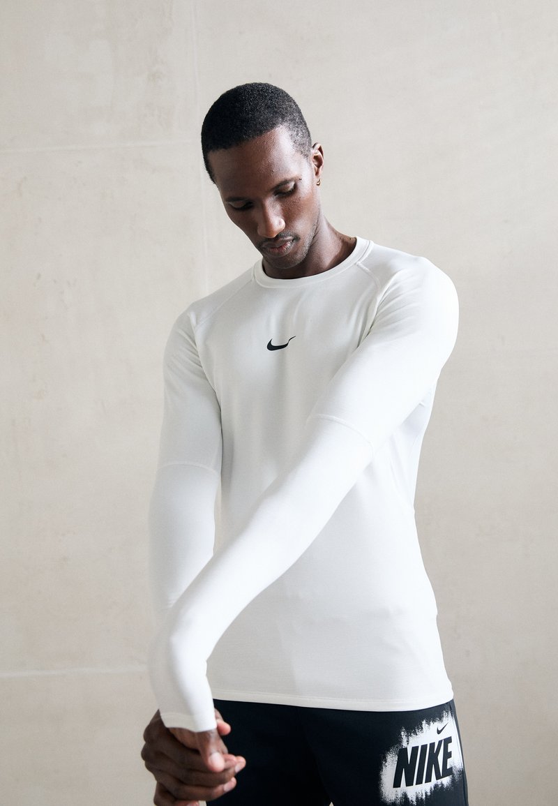 Langermet hvit idretts skjorte med en svart Nike-logo på brystet, kombinert med svarte shorts med en iøynefallende hvit Nike-trykk.