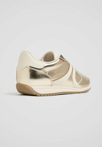 Gouden metallic sneaker met getextureerde beige accenten, vetersloze ontwerp, lichtgewicht zool en gevoerde binnenkant voor comfort.