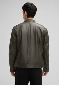 Olivegrüne Lederjacke mit glatter Oberfläche, taillierter Passform und subtilen Nahtdetails; sie verfügt über einen Kragen und geknöpfte Manschetten.