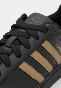 Black leather sneaker with three tan stripes. Features textured laces and tongue embossed with logo. Stitched detailing on the sides.
