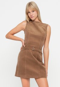 Braunes Corduroykleid mit tailliertem Oberteil, hohem Ausschnitt, ärmellosem Design und einem Gürtel in der Taille. Glatte Textur und knielanger Saum.