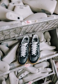 Baskets noires et blanches avec des lacets blancs placées sur des étagères en métal remplies de différents embauchoirs blancs étiquetés avec diverses tailles.