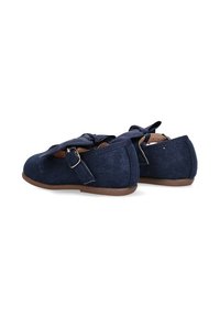 Zapatos de tela azul marino con suela plana, puntera redondeada y un detalle de lazo. Acentos de hebilla metálica en el lateral, parte superior texturizada con ligero brillo.