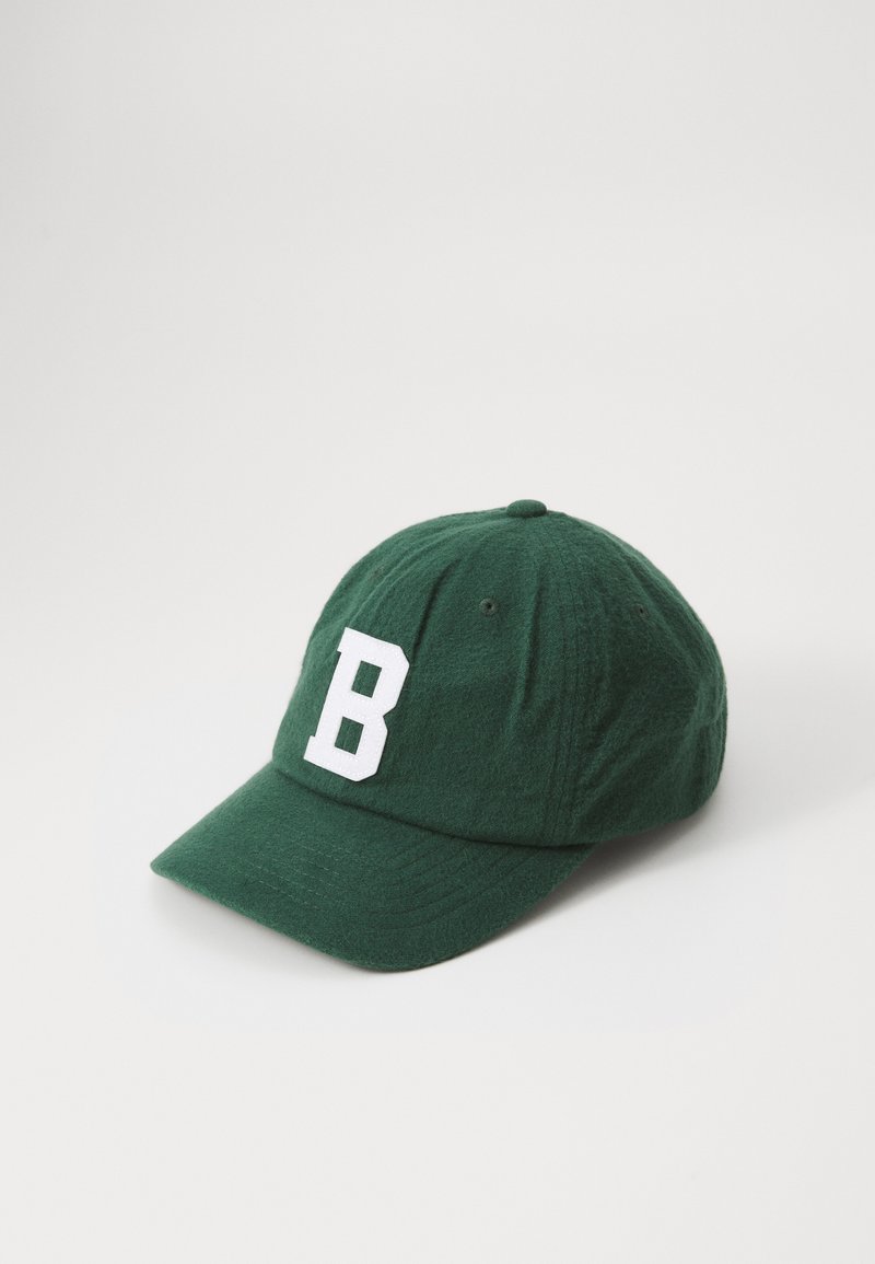 Mørkegrønn baseballcaps i myk stoff med en hvit bokstav "B" foran. Designet inkluderer en buet brem og ventilasjons hull.