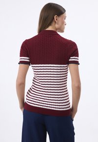 Polo en tricot rayé bordeaux et blanc avec un design en câble texturé, manches courtes, et un col et un ourlet côtelés.