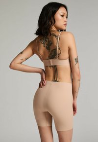 Beige sporttop met dunne bandjes en een open rug, gecombineerd met bijpassende shorts tot halverwege de dij; gladde stof, minimale naden en een aansluitend ontwerp.