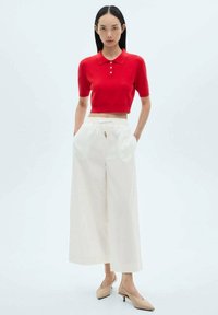 Rode cropped polo sweater met korte mouwen, gecombineerd met witte wijde broek en beige slingback-hakken, met een knoopdetail bij de kraag.