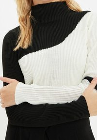 Suéter de cuello alto de canalé con un diseño en bloques de color negro y blanco, con texturas contrastantes y mangas largas.