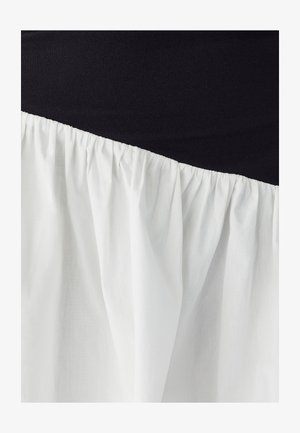 Crni top s glatkom teksturom i bijelim nabranim materijalom na dnu, stvarajući kontrastni dizajn blokova boja.