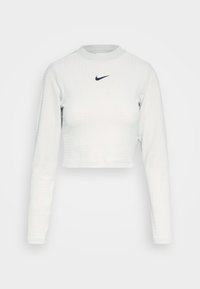 Långärmad, cropped topp i texturerad vit tyg med rund halsringning och en liten svart Nike-logotyp på bröstet.