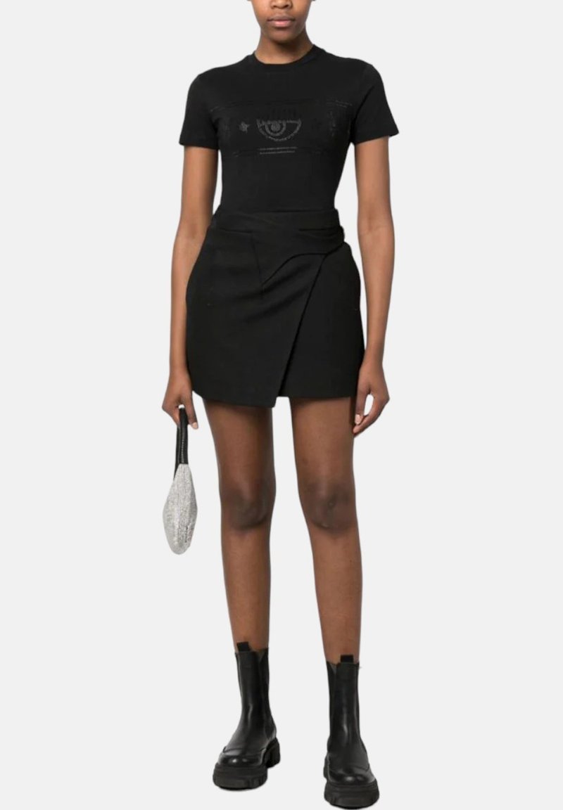 Schwarzes, kurzärmliges, tailliertes T-Shirt mit Logodetail, kombiniert mit einem schwarzen Wickelrock. Es hat eine elegante Silhouette und schwarze Stiefeletten.