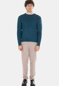 Maglione verde acqua lavorato a maglia con motivo strutturato, abbinato a pantaloni beige chiaro e scarpe nere. Scollo rotondo e silhouette aderente.