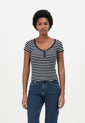 Stripet t-skjorte med korte ermer i marineblå og hvit, med rund hals og tre knapper. Kombinert med mørkeblå denimjeans.