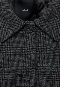 Szary płaszcz w kratę z kołnierzem, wykonany z teksturowanej tkaniny, z pojedynczym zapięciem na guzik z przodu. Widoczna metka MNG.