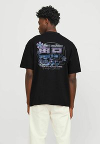 Sort T-shirt med korte ærmer, der har et stort grafisk print på ryggen med blomsteraccenter og japansk tekst, der står "Tokyo Kultur, Kirsebærblomst."