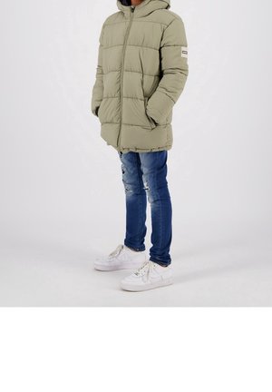 Doudoune verte olive, fermeture à zip, motif matelassé. Portée avec un jean bleu déchiré et des baskets blanches.