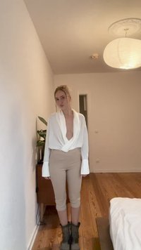 Blusa blanca de manga ancha, combinada con leggings beige cortos y botas oscuras hasta el tobillo, sobre un fondo neutro.