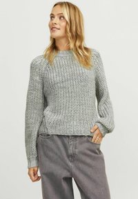 Light gray knitted sweater with a high neckline, ribbed cuffs, and a loose fit, paired with dark gray loose-fit jeans.