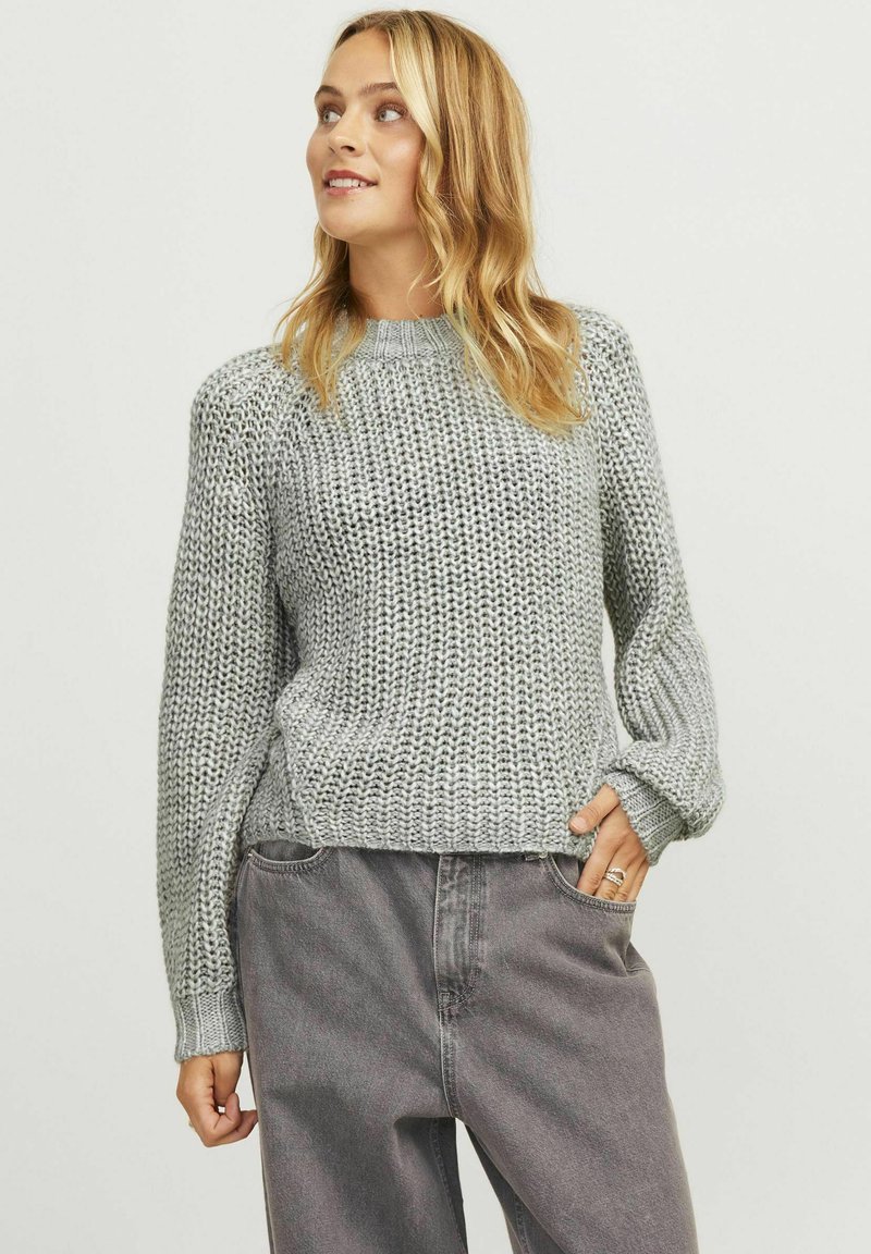 Light gray knitted sweater with a high neckline, ribbed cuffs, and a loose fit, paired with dark gray loose-fit jeans.