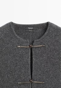 Cardigan grigio in lana con scollatura rotonda, due chiusure a bottone con cinturini in pelle e superficie strutturata. Etichetta di cura visibile all'interno.