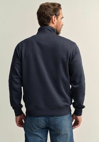 Navy blue sweatshirt with a high collar, made of soft fabric, featuring long sleeves and a relaxed fit, paired with blue denim jeans.