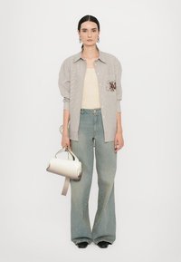 Camicia a righe con maniche oversize, top beige, jeans a gamba larga di colore blu chiaro e borsa crema con manico corto.