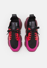 Baskets à lacets avec une tige noire, des accents rouges et roses, un matériau texturé, et des semelles épaisses et massives au design robuste.