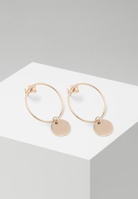 Orecchini a cerchio in oro con pendente a disco circolare. Presentano una finitura liscia e una chiusura sicura. Design minimalista con una texture leggera e lucida.