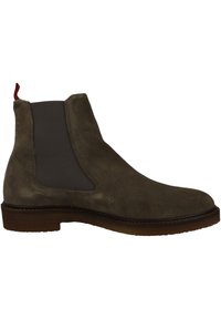 Botas Chelsea para hombre, de gamuza oliva con paneles elásticos, puntera redonda, suela de goma marrón y tirador rojo en el talón. Textura suave.