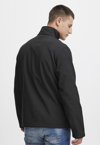 Sort softshell-jakke med høj krave, glat tekstur og lige snit. Bagsiden viser minimale detaljer og sømme.