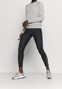 Sweat-shirt gris à manches longues, associé à un legging noir à rayures avec un logo, et des chaussures de sport grises avec une semelle blanche.