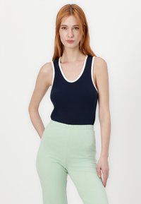 Ναυτικό αμάνικο τοπ με λευκή λεπτομέρεια, που διαθέτει στρογγυλή λαιμόκοψη. Συνδυάζεται με ανοιχτό πράσινο παντελόνι με ελαστική μέση, που αναδεικνύει μία εφαρμοστή σιλουέτα.