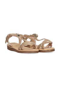 Sandalias de tiras beige con suela plana, que cuentan con detalles entrecruzados y correa en el tobillo, fabricadas con material texturizado y acentos metálicos.