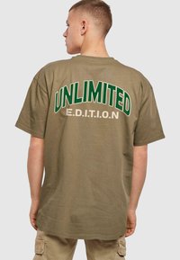 Oliven grøn t-shirt med korteærmer, med stort hvidt og grønt "UNLIMITED" tekst og "E.D.I.T.I.O.N" nedenunder. Udekoreret stofstruktur.