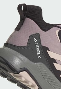 Šedá a černá atletická bota s texturovaným svrškem, zesílenou patou a výrazným brandingem. Vzorovaná podrážka navržená pro trakci.