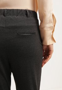 Zwarte stretchbroek met een slank ontwerp en een achterzak. De stof lijkt zacht en enigszins gestructureerd.