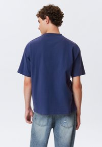 Mørkeblå, kortærmet t-shirt med en afslappet pasform, lavet af blødt stof; kombineret med lyseblå, slidte denimjeans.