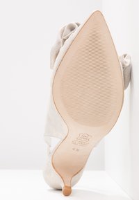 Chaussure à talons avec un dessus en argent texturé, ornée d'une accent en forme de fleur, à bout pointu et semelle en caoutchouc de couleur claire avec des rainures.