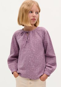 Blusa lilla con scollatura rotonda e dettaglio di fiocco, caratterizzata da un motivo floreale testurizzato e maniche arricciate a sbuffo.