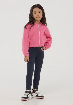 Hoodie cropped rosa con zip e tasca frontale, abbinato a leggings blu navy e sneakers nere con dettagli bianchi e rosa.